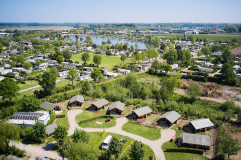 Vista aérea de tiendas safari en Camping Betuwestrand, Países Bajos, con lago y zonas verdes de fondo.