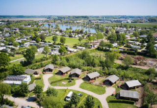 Vista aérea de tiendas safari en Camping Betuwestrand, Países Bajos, con lago y zonas verdes de fondo.