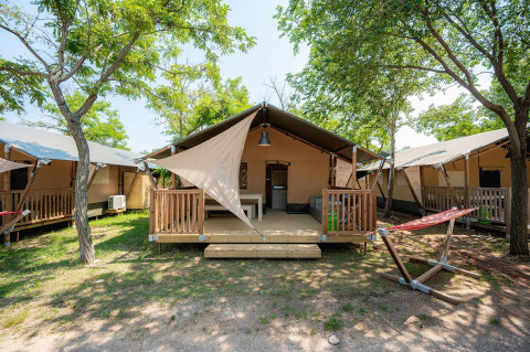 Tienda safari Villatent Outback con porche de madera, hamaca y árboles en campamento soleado.