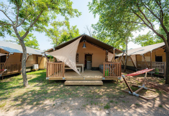 Safari tent Villatent Outback with wooden porch, hammock, and trees on a sunny campground setting.