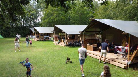 Familias disfrutan actividades al aire libre junto a cabañas de lona en Camping de Beukenhof, Drenthe, Países Bajos.