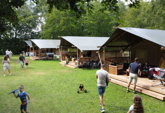 Familias disfrutan actividades al aire libre junto a cabañas de lona en Camping de Beukenhof, Drenthe, Países Bajos.