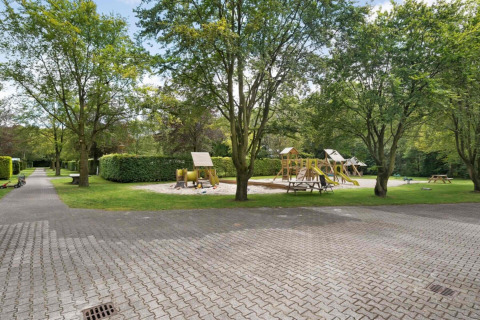 Área de juegos rodeada de árboles y césped en Camping de Beukenhof, parque vacacional en Drenthe, Países Bajos.