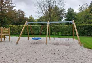 Parco giochi con altalene e sabbia, circondato da siepi al Camping de Beukenhof, Drenthe, Paesi Bassi.