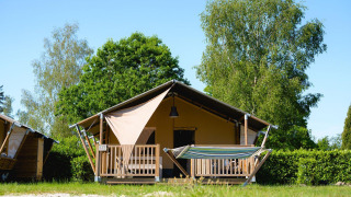 Safari-Zelt Villatent Outback mit Hängematte auf Camping de Schatberg in den Niederlanden, umgeben von Bäumen.