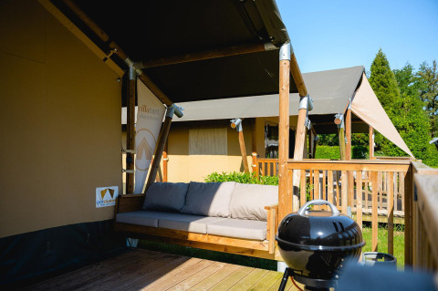 Tienda safari Villatent Outback con terraza, sofá y barbacoa en Camping de Schatberg en los Países Bajos.
