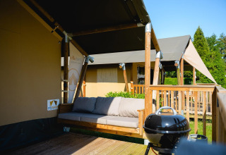 Tienda safari Villatent Outback con terraza, sofá y barbacoa en Camping de Schatberg en los Países Bajos.