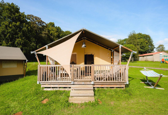 Tienda safari Villatent Outback en Camping La Colline, Bélgica, con porche de madera y hamaca exterior.