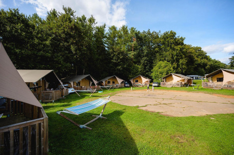 Tiendas tipo safari y hamacas en Camping La Colline, Bélgica, rodeadas de vegetación y bosque trasero.